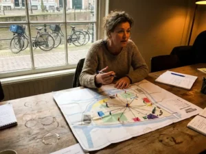 Nederlandse evenementencoördinator plant festivaltransport met kaart en gekleurde pinnen op houten tafel in Amsterdams kantoor