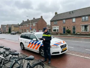 Nederlandse verkeersagent in uniform met klembord naast politieauto op straat met bakstenen huizen en fietspaden
