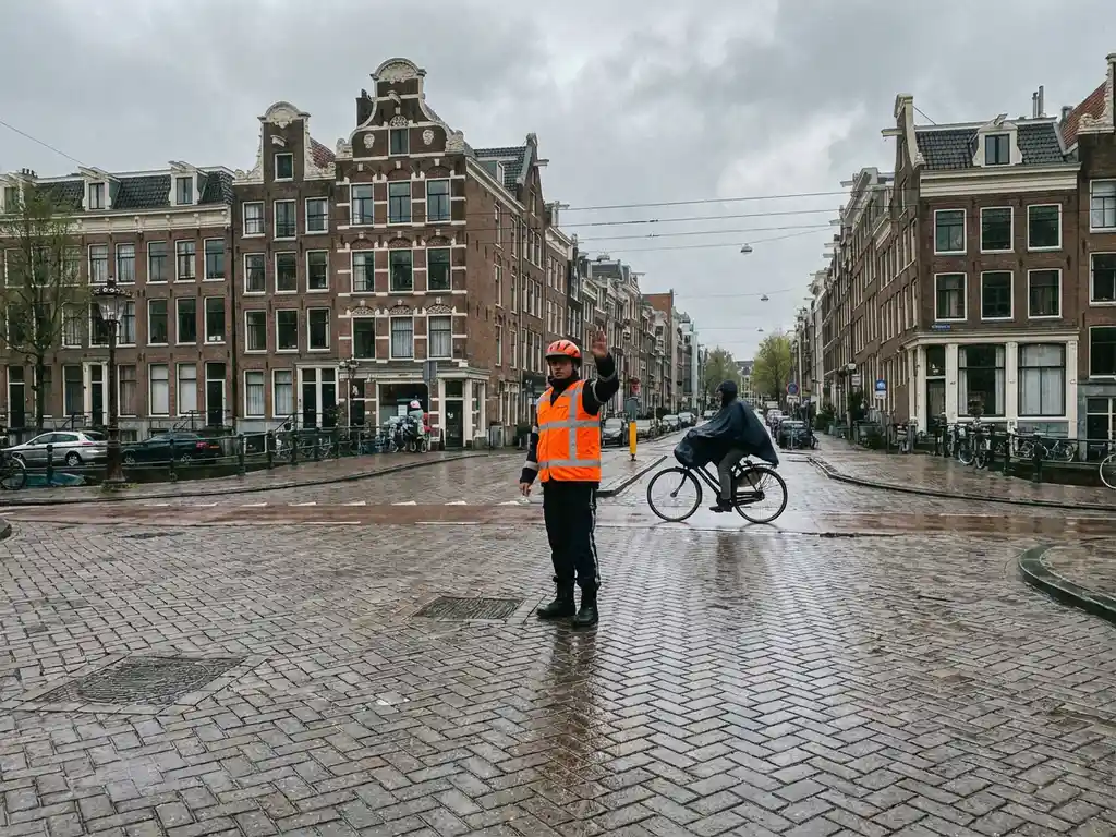 Verkeersregelaar in oranje reflecterend vest dirigeert verkeer op Nederlandse kruising met traditionele panden