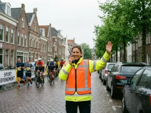 Verkeersregelaar in oranje veiligheidsvest dirigeert verkeer op Nederlandse straat met fietsers en joggers op achtergrond