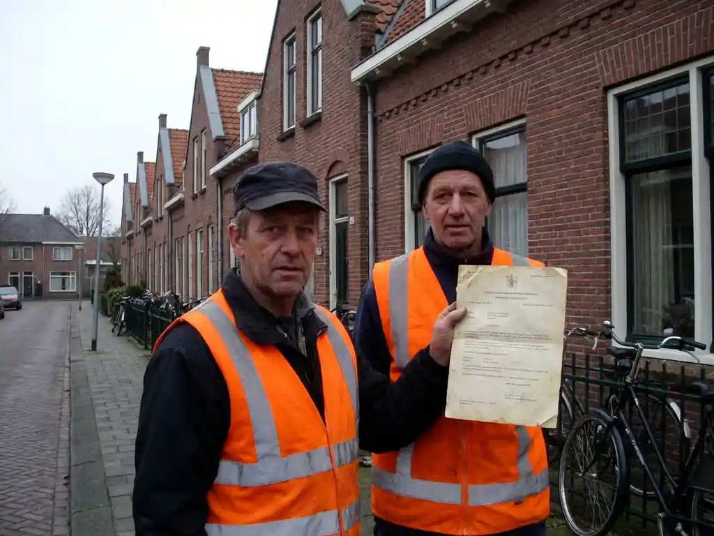 Nederlandse verkeersregelaar in oranje veiligheidsvest toont certificaat bij bakstenen huizen en fietsen