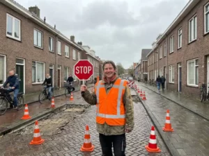 Verkeersregelaar in oranje hesje met stopbord op Nederlandse woonstraat met bakstenen huizen en wegwerkzaamheden