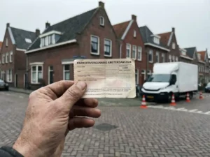 Hand houdt verkeersvergunning vast op Nederlandse straat met rode bakstenen huizen en bezorgwagen op achtergrond