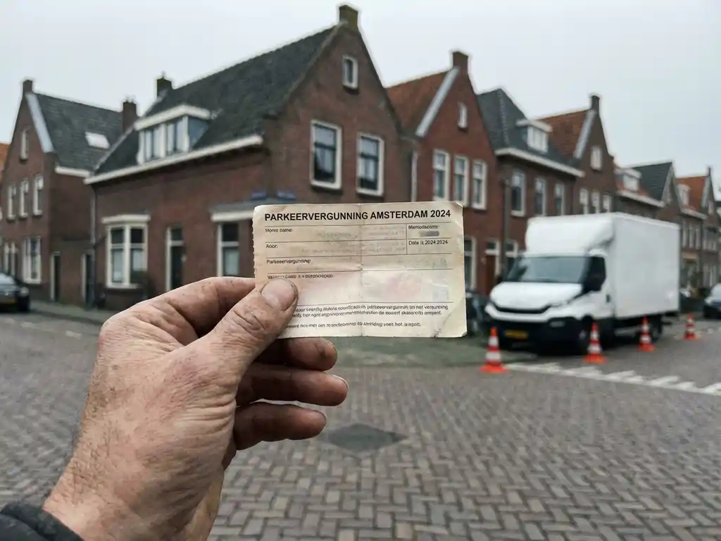Hand houdt verkeersvergunning vast op Nederlandse straat met rode bakstenen huizen en bezorgwagen op achtergrond